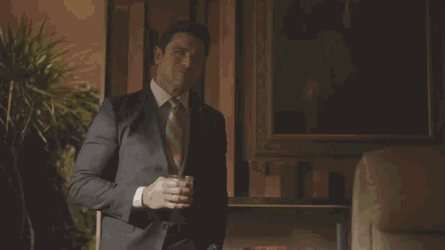 a man in a suit and tie holds a glass