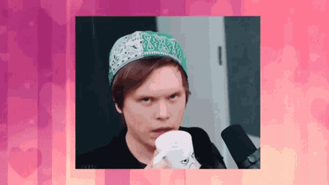 a young man wearing a bandana and a hat is drinking from a mug .