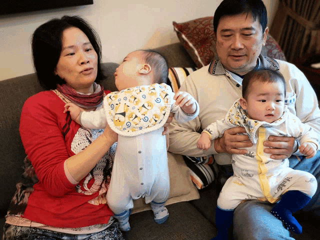 a man and a woman sitting on a couch with two babies