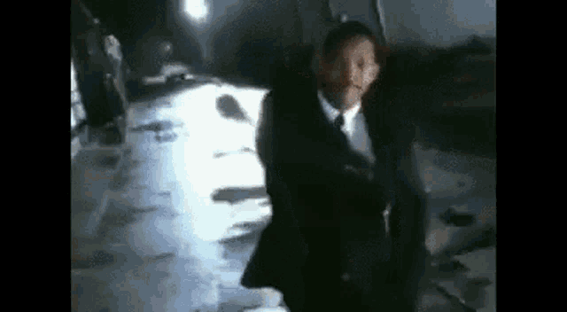 a man in a suit and tie is standing in a dark room with a gun .