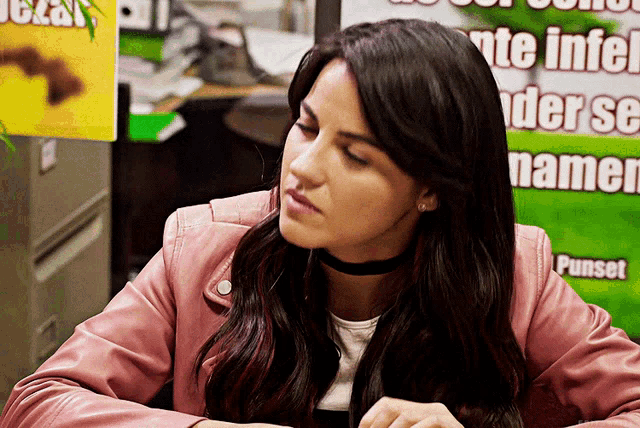 a woman in a pink jacket sits in front of a green sign that says punset