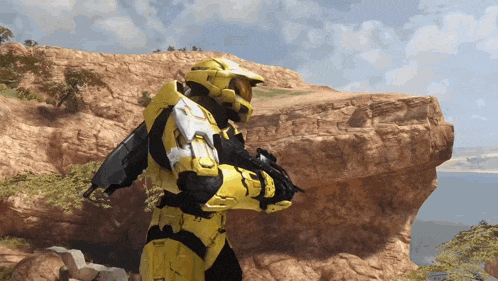 a man in a yellow armor is standing on top of a rocky hill near a body of water