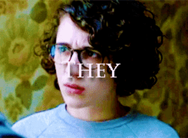a person with curly hair wearing glasses and the word they behind them