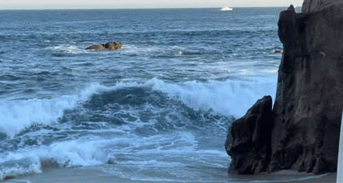 waves crashing on a rocky shore with a boat in the distance