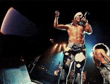 a shirtless man sings into a microphone on stage