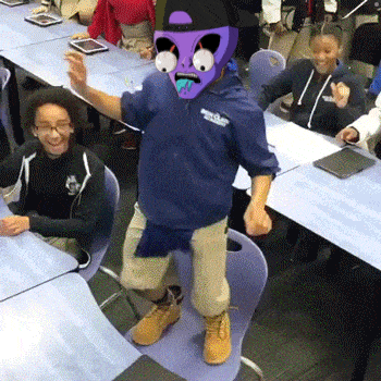 a boy wearing a purple mask is dancing in front of a group of students