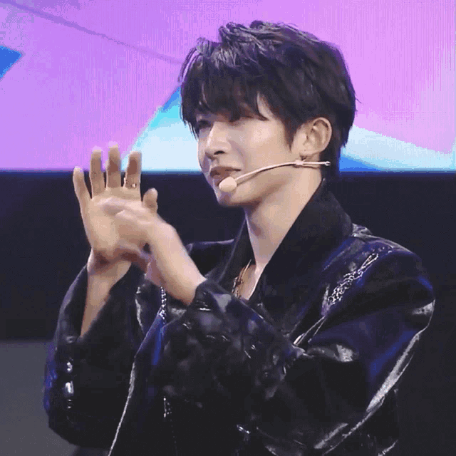a man wearing a black jacket and a microphone is clapping