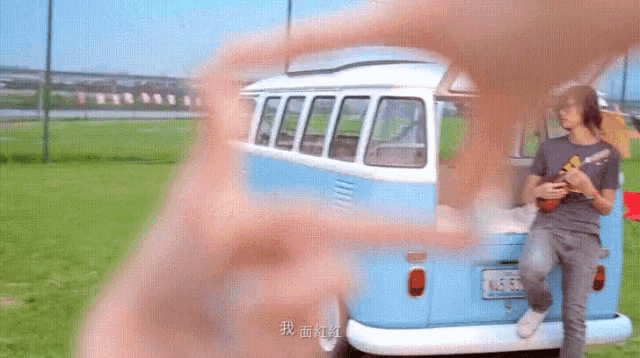 a man playing an ukulele in front of a blue and white van .