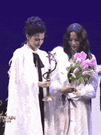 two women standing next to each other holding flowers and a trophy with the year 2020 on the bottom