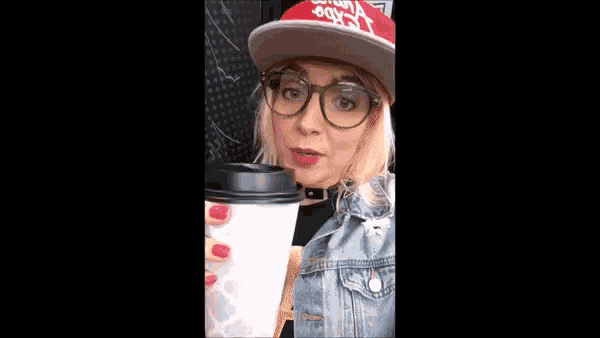 a woman wearing a red hat and glasses is drinking out of a cup