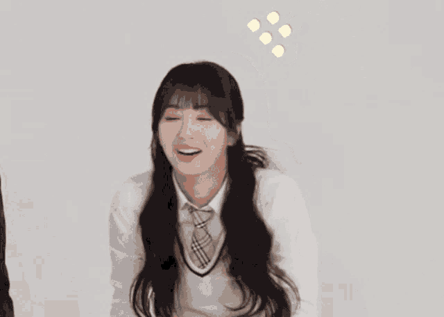 a girl in a white shirt and plaid tie is smiling and looking at the camera