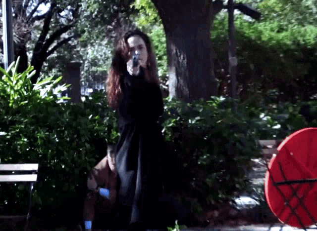 a woman in a black coat is pointing a gun in a park