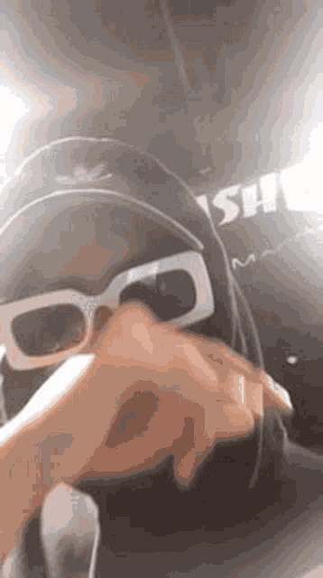 a person wearing a hat and sunglasses is covering their face with their hand .