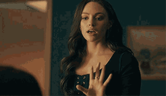 a woman in a black dress is making a hand gesture while standing in a room .