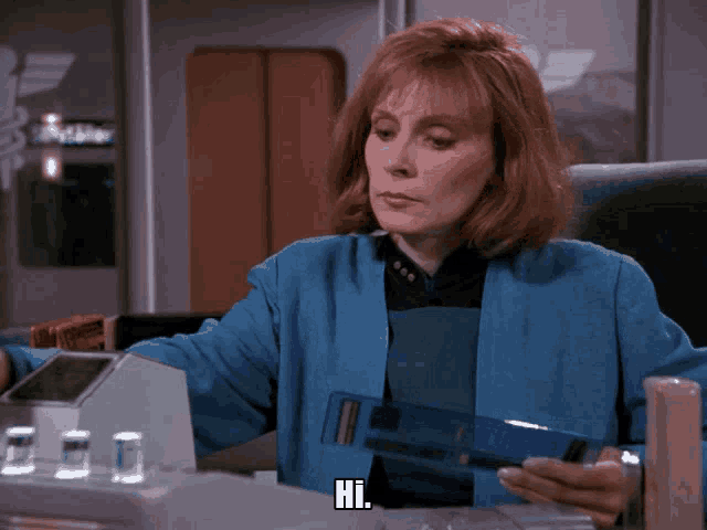 a woman in a blue jacket is sitting at a desk with the word hi on the screen