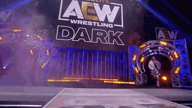 a wrestler is walking through a tunnel in front of a aew wrestling dark sign .