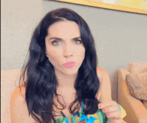 a woman with long black hair is sitting on a couch making a funny face