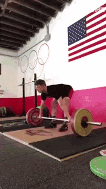 a man is lifting a barbell in a gym with an american flag hanging on the wall .