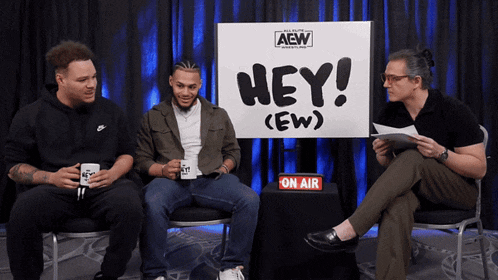 three men sit in front of a sign that says " hey "