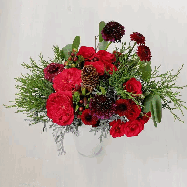a bouquet of red flowers and pine cones in a white vase