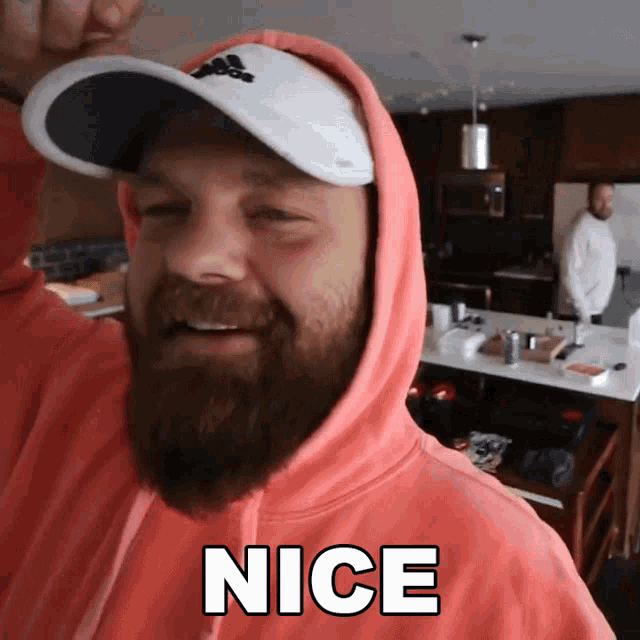 a man with a beard is wearing a pink hoodie and a white hat with the word nice on it