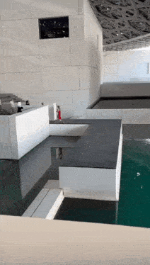 a woman in a red dress is standing on a ledge next to a pool