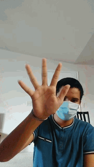 a man wearing a blue shirt and a face mask holds up his hand