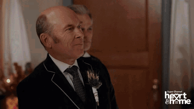 a man in a suit and tie stands in front of a super channel heart & home ad