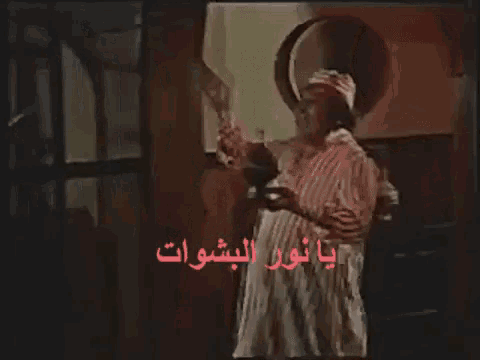 a man in a striped shirt is standing in a dark room with arabic writing on the bottom right