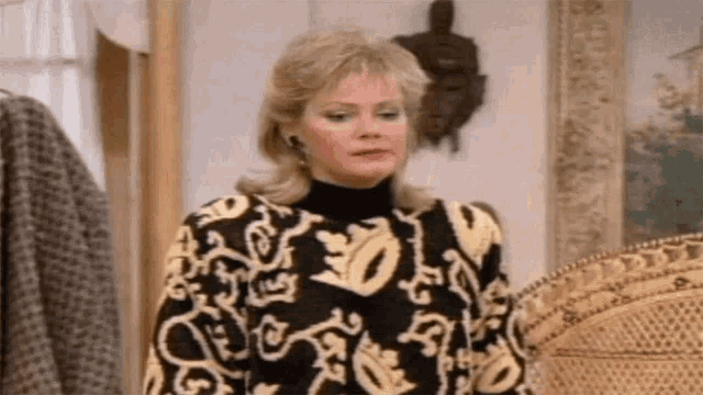 a woman wearing a black and yellow sweater is standing in front of a wicker chair .