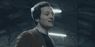 a man in a brown jacket is dancing in a dark room with lights on .