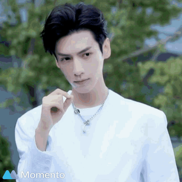 a man wearing a white shirt and a necklace is standing in front of a momento logo