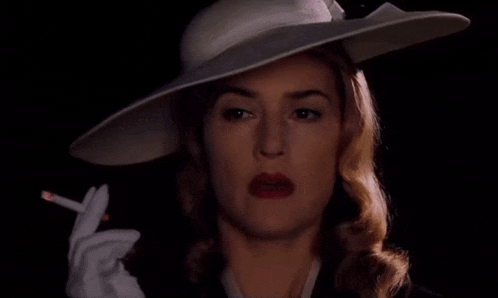 a woman in a white hat is smoking a cigarette and says " i 'm back you bastards "
