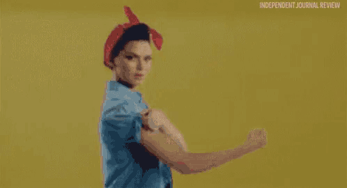 a woman in a blue shirt and red headband is flexing her arms .
