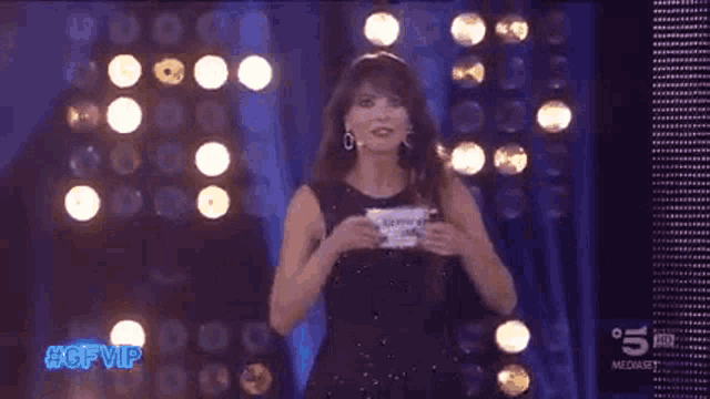a woman in a black dress is holding a sign that says rickyi vella cam