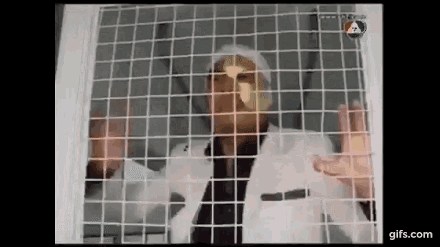 a man in a white suit is behind a fence with a gold mask on his face .