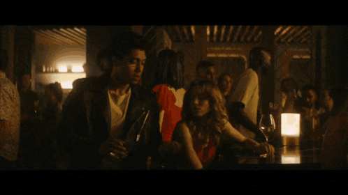 a man in a leather jacket talks to a woman in a bar