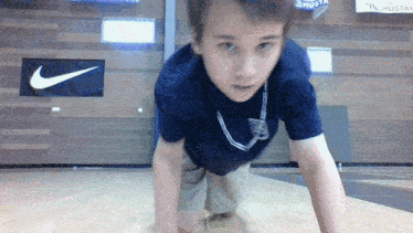a boy in a blue shirt is doing push ups in front of a nike banner