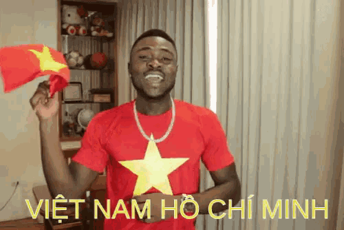 a man wearing a red shirt with a yellow star on it holds a small flag in his hand and says viet nam ho chi minh