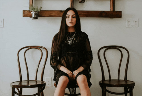 a woman in a black dress sits on a chair with her legs crossed
