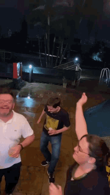 a group of people are dancing in front of a swimming pool at night