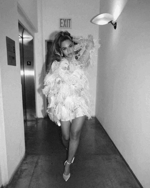 a woman in a white feathered dress is standing in a hallway with an exit sign on the wall behind her