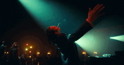 a man smoking a cigarette in a dark room with his arms outstretched
