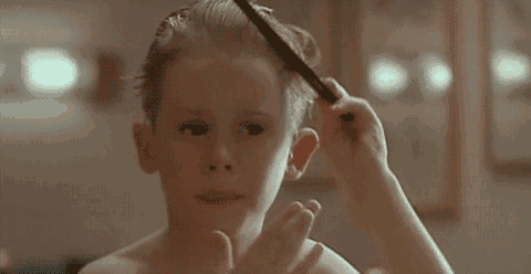a young boy is brushing his hair with a comb in front of a mirror .