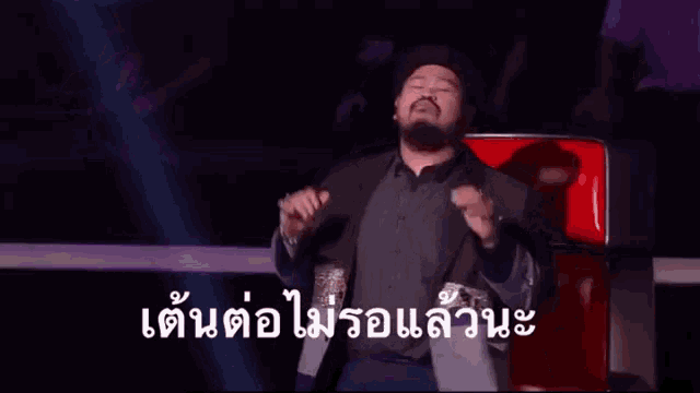 a man with a beard is sitting in a red chair with a foreign language caption