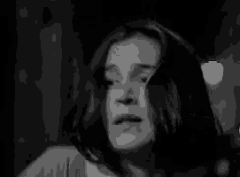 a black and white photo of a woman with long hair making a scary face .