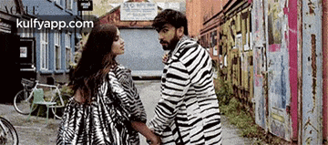 a man and a woman are standing next to each other holding hands . the man is wearing a zebra print jacket .