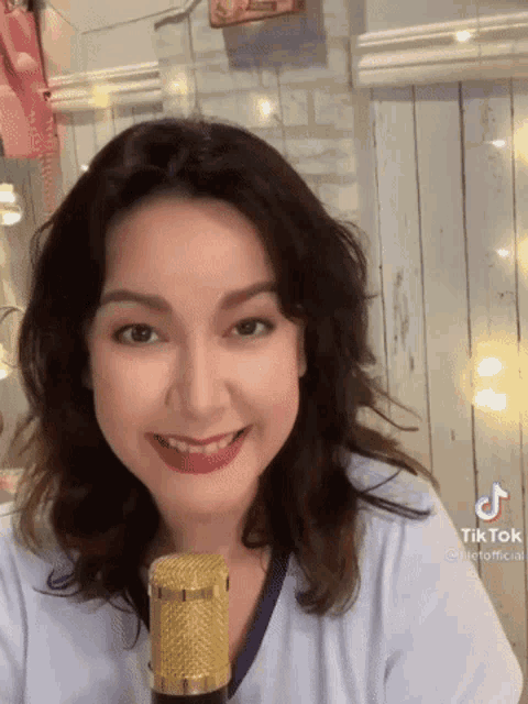 a woman in a white shirt is smiling in front of a gold microphone