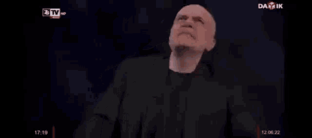 a man in a black suit is giving a speech on a tv show