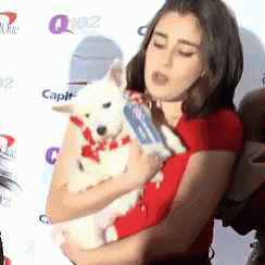 a woman in a red shirt is holding a white dog in her arms